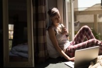 Femme utilisant un ordinateur portable tout en prenant un café à la maison . — Photo de stock