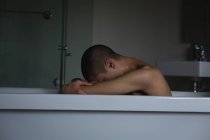 Depressed young man sitting in bathtub at bathroom — Stock Photo