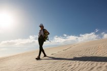 Female hiker with backpack walking on sand on a sunny day — Stock Photo