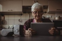 Пожилая женщина пользуется цифровым планшетом на кухне дома — стоковое фото