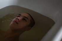Jeune homme réfléchi relaxant dans la baignoire à la salle de bain — Photo de stock