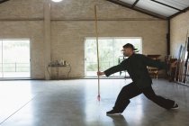 Karate fighter practicing with long pole in fitness studio. — Stock Photo