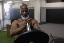 Senior man exercising with barbell in fitness studio. — Stock Photo