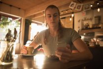 Людина використовує мобільний телефон, маючи каву в кафетерії — стокове фото