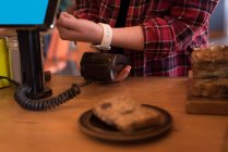 Клієнт здійснює оплату за допомогою смарт-годинника за лічильником у кафе — стокове фото