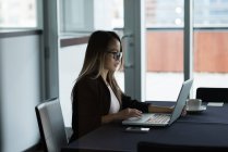 Азиатская бизнесвумен в очках работает над ноутбуком в офисе — стоковое фото