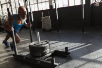 Déterminé homme âgé poussant traîneau de poids dans le studio de fitness . — Photo de stock