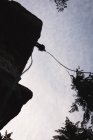Vista de baixo ângulo do alpinista escalando o penhasco rochoso contra o sol — Fotografia de Stock