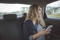 Junge Geschäftsfrau benutzt Handy und schaut im Auto aus dem Fenster — Stockfoto