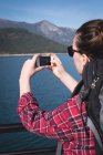 Вид ззаду жінки, що фотографує мобільний телефон у сонячний день — стокове фото