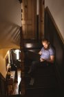 Человек, использующий свой ноутбук, сидя дома на лестнице — стоковое фото