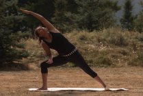 Подходящая женщина, выполняющая упражнения на растяжку на открытом воздухе в солнечный день — стоковое фото