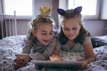 Siblings using digital tablet on bed in bedroom at home — Stock Photo