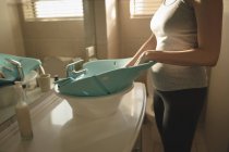 Giovane mamma mettendo seggiolino da bagno per bambini nel lavandino del bagno a casa — Foto stock