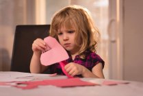 Ragazza che prepara decorazione a forma di cuore con carta artigianale a casa — Foto stock