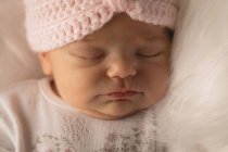 Newborn baby in knitted hat sleeping on fluffy blanket at home. — Stock Photo