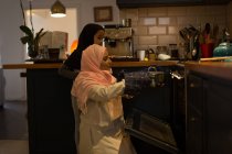 Мусульманская женщина и дочь используют духовку на кухне дома — стоковое фото