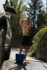 Мальчик играет с водой, когда моет машину на улице гаража — стоковое фото
