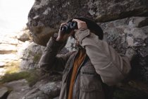 Hiker looking through binoculars from the cave — Stock Photo