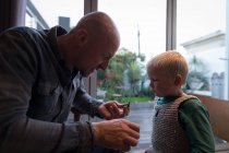 Отец учит сына вязать булавкой и ниткой дома — стоковое фото