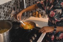 Donna che prepara il cibo in padella sui fornelli in cucina . — Foto stock