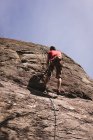 Низкий угол обзора восхождения альпиниста по скалистой скале — стоковое фото