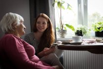 Lächelnde Enkelin interagiert mit Großmutter im heimischen Wohnzimmer — Stockfoto
