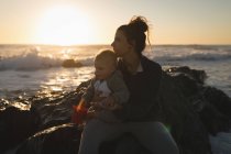 Mãe e filho relaxando na rocha na praia durante o pôr do sol — Fotografia de Stock