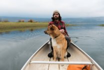 Uomo remo canoa nel fiume con il suo cane a bordo — Foto stock