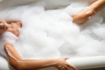 Femme prenant un bain avec mousse dans la baignoire . — Photo de stock