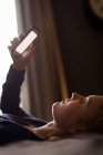 Nahaufnahme einer jungen Frau, die sich mit ihrem Handy auf das Bett legt — Stockfoto