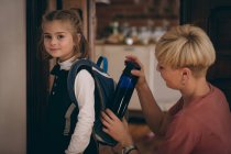 Mother keeping water bottle in daughter bag pack at home — Stock Photo
