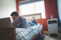 Молодой человек лежит на фронте и использует ноутбук в спальне . — стоковое фото