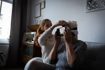 Внучка помогает бабушке с гарнитурой виртуальной реальности дома — стоковое фото
