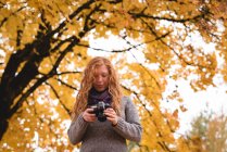 Femme vérifiant les photos dans l'appareil photo numérique dans le parc d'automne — Photo de stock