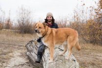 Усміхнений чоловік і його собака сидять на дерев'яному колоді — стокове фото