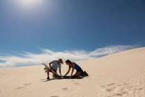 Couple vérifiant sandboard dans dune de sable au désert — Photo de stock