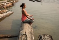 Стройная женщина, сидящая в позе медитации на упавшем стволе дерева в солнечный день — стоковое фото