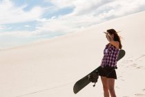 Woman with sandboard standing in the desert on a sunny day — Stock Photo