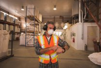 Uomo in abbigliamento da lavoro protettivo con smartwatch in fabbrica — Foto stock
