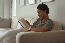 Femme lisant un livre sur canapé à la maison — Photo de stock