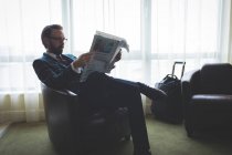 Geschäftsmann liest Zeitung auf Sessel im Hotel — Stockfoto