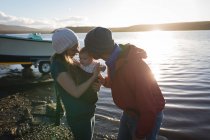 Padre besando bebé cerca de la orilla del río al atardecer . - foto de stock