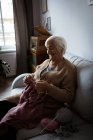 Mujer mayor tejiendo lana en la sala de estar en casa - foto de stock