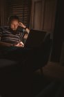 Крупним планом чоловік у темній кімнаті, сидячи на дивані, використовуючи свій ноутбук вдома — стокове фото