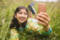 Menina feliz tomando selfies enquanto deitado na grama — Fotografia de Stock