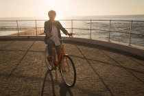 Mujer mayor montando bicicleta en el paseo marítimo en un día soleado - foto de stock