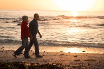 Casal sênior andando na praia durante o pôr do sol — Fotografia de Stock