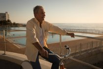 Pensativo hombre mayor sentado en bicicleta en el paseo marítimo - foto de stock