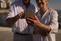 Couple sénior utilisant un téléphone portable sur la promenade — Photo de stock